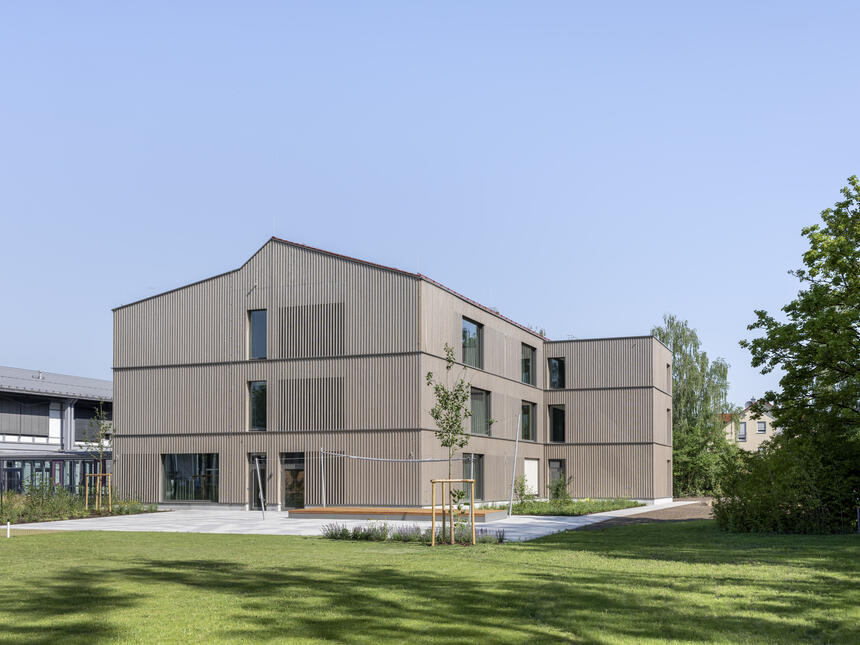 Erweiterungsbau Gymnasium Ismaning mit Holzfassade, Schulhof, Rasenfläche und blauem Himmel