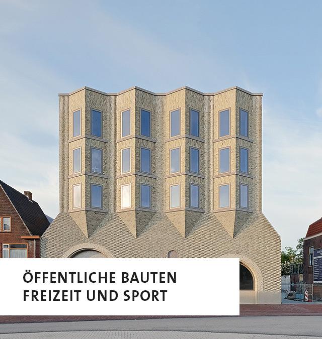 Ein Gebäude in grauem Backstein, unten links die Aufschrift: Öffentliche Bauten, Freizeit und Sport