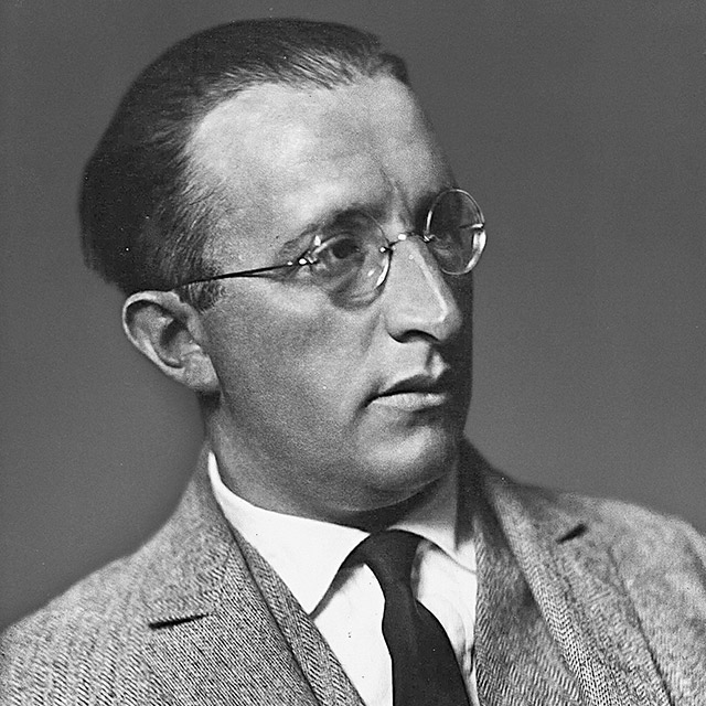 Ein Schwarz-Weiß-Porträt von Erich Mendelsohn. Er trägt Anzug, Krawatte und Brille und blickt Richtung rechtem Bildrand.
