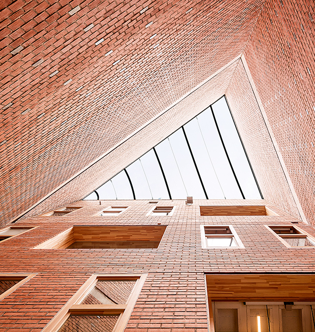 Eine Architekturfotografie des Civic Center der Harquitectes: Der Blick geht einen dreieckigen Schacht eingefasst von roten Backsteinwänden entlang und endet an einem dreieckigen Fenster im Dach.