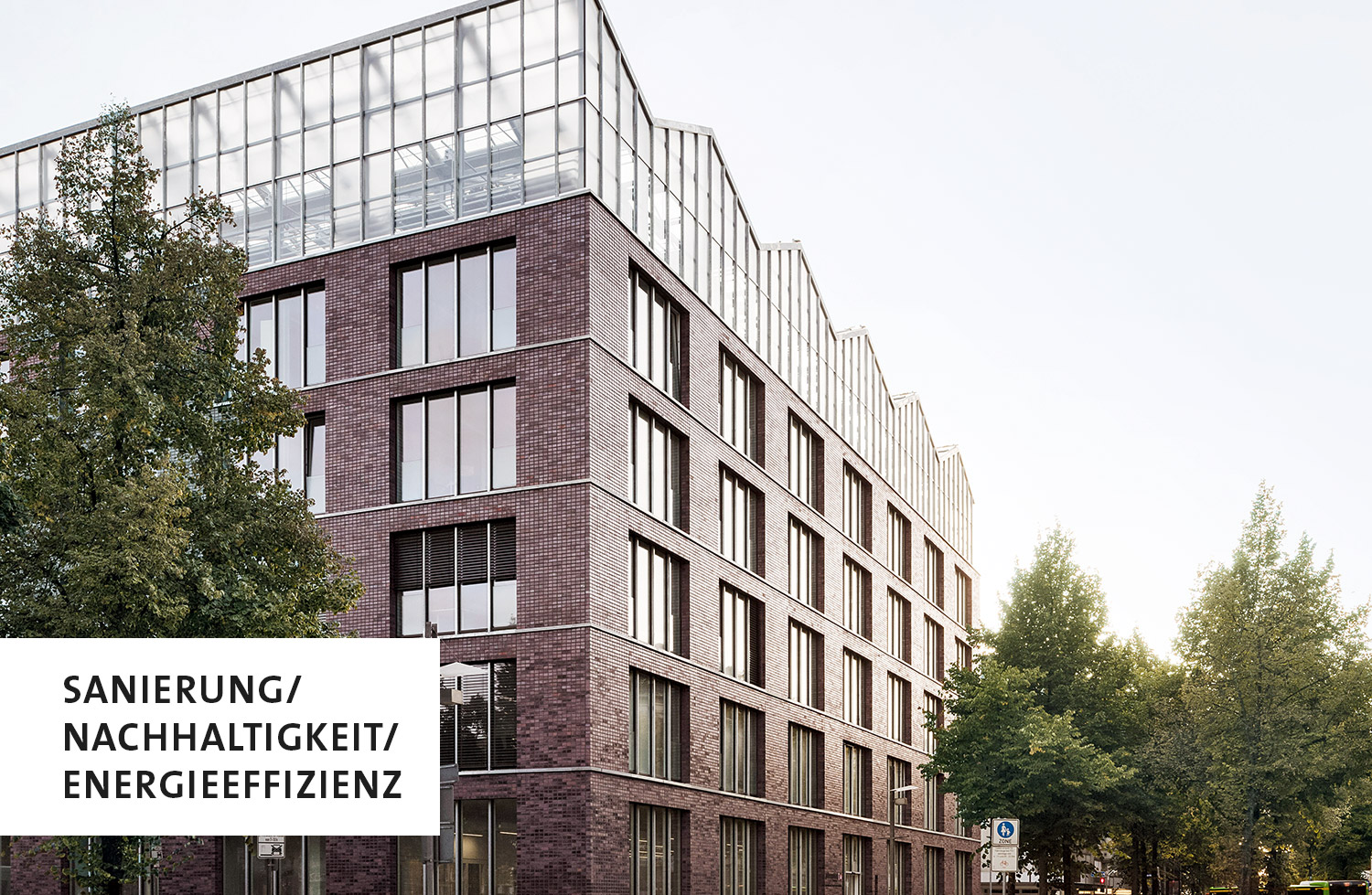 Ein Gebäude mit rotbraunem Backstein und einem gläsernen Dachaufbau, unten links die Aufschrift: Sanierung/Nachhaltigkeit/Energieeffizienz
